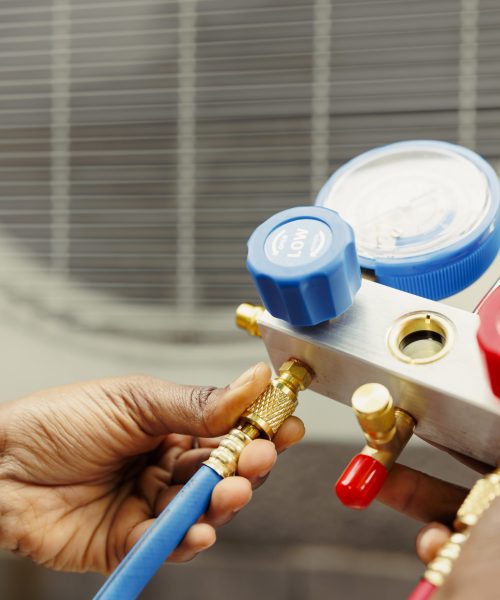 Close up of professional worker holding pressure indicators used for checking air conditioner freon tank in need of maintenance. Licensed serviceman using manifold gauges to check refrigerant levels
